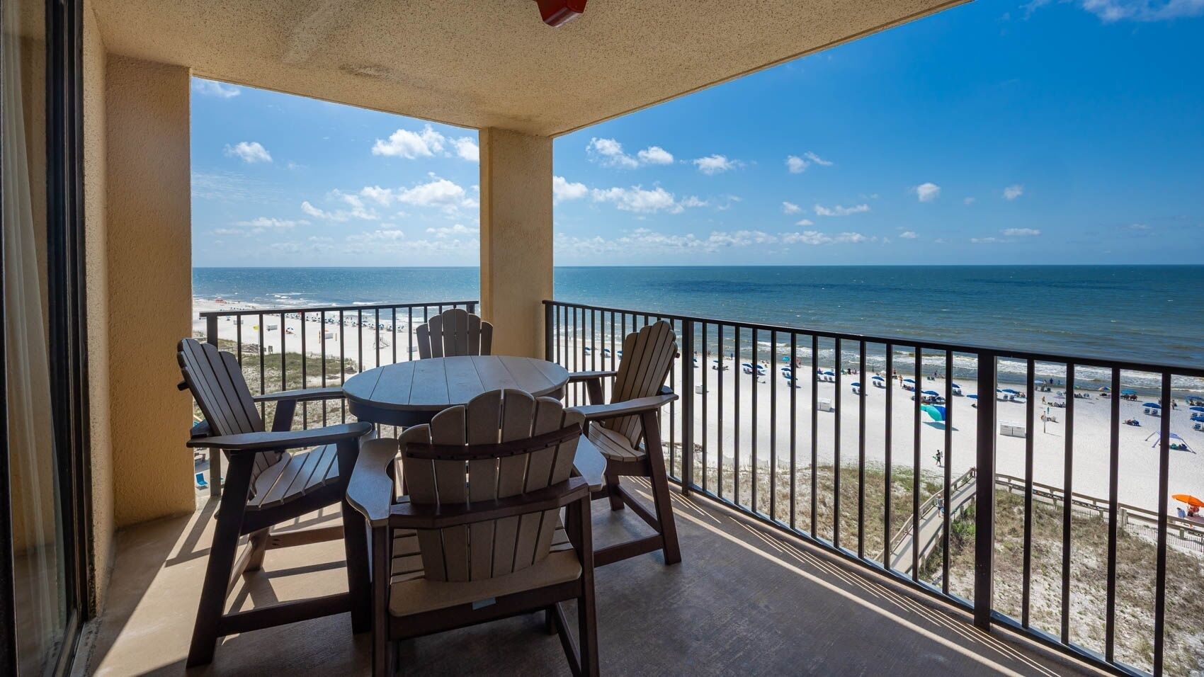 A balcony with a view of the beach, equipped with a table and chairs.