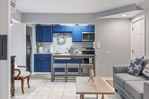 Eine moderne Küche mit blauen Schränken, einem Esstisch mit Stühlen und einem grauen Sofa mit Kissen in Sternenmuster.