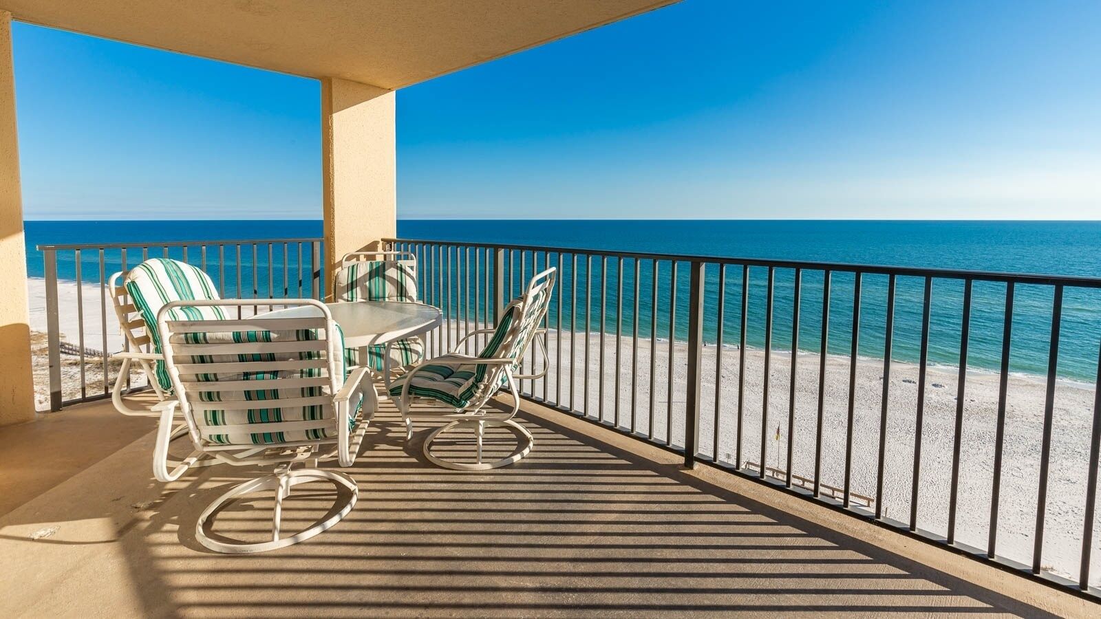 A balcony with a table and chairs, overlooking a beach and the ocean.