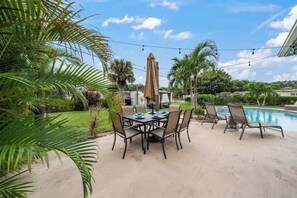 Una terrazza esterna con tavolo e sedie, una piscina e palme.