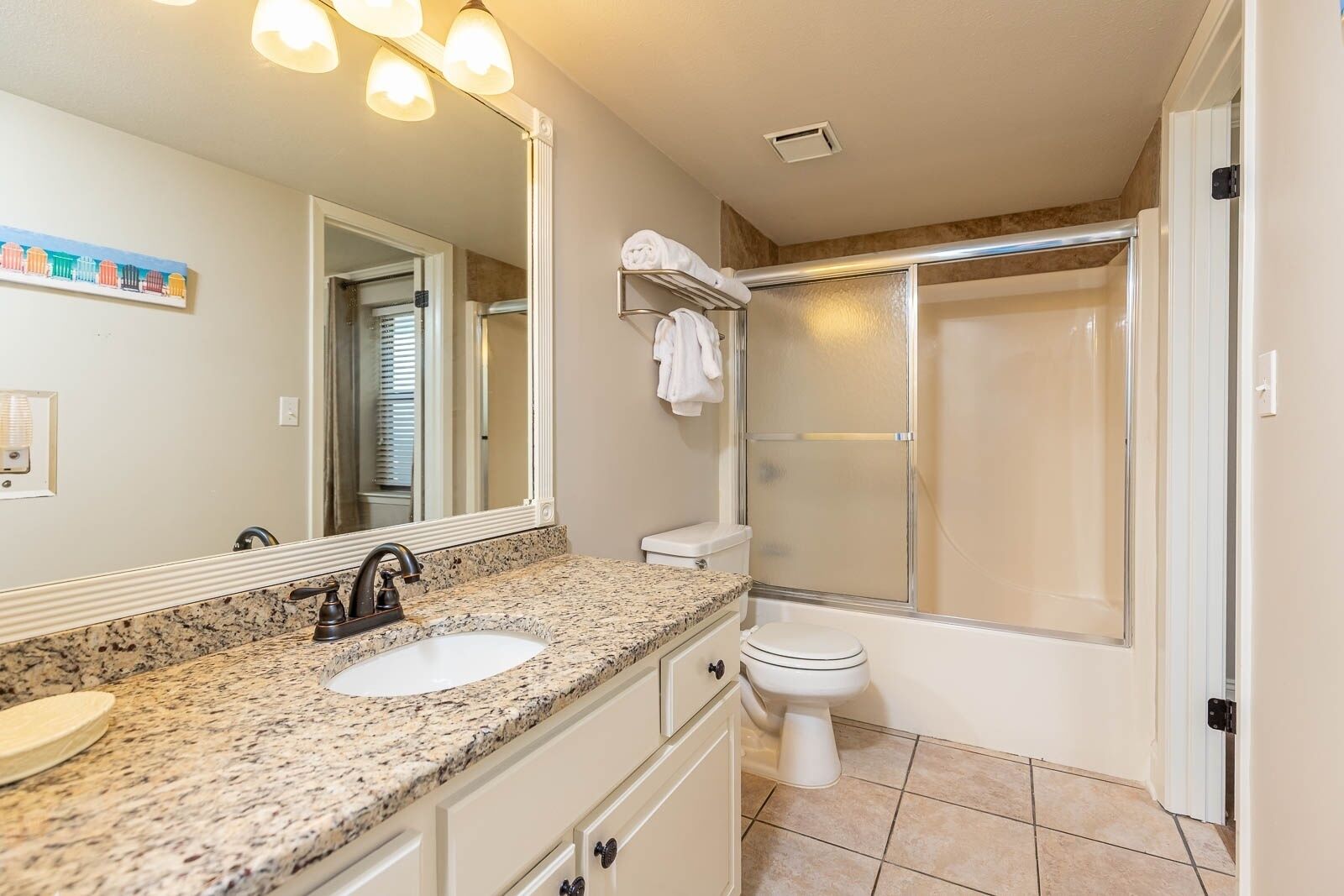 A bathroom with a granite countertop, a sink, a toilet, a shower with a glass door, and a large mirror.