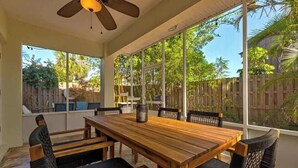 A covered patio with a wooden table and chairs, large windows, and a ceiling fan. - 3BR Beach Getaway w Balcony (Cape Canaveral)