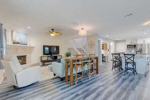 Ein modernes Wohnzimmer mit Kamin, eine Essecke mit Holztisch und Stühlen, eine Küche mit weißen Schränken und eine Treppe, die zu einer weiteren Ebene führt.