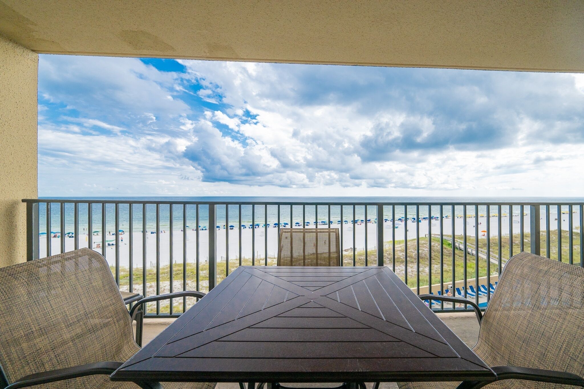 A balcony with a view of the beach, a table, and two chairs.