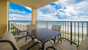A balcony with a table and chairs, overlooking a beach with a view of the ocean and clouds. - Phoenix V 412 3 Bedroom Condo (Orange Beach)