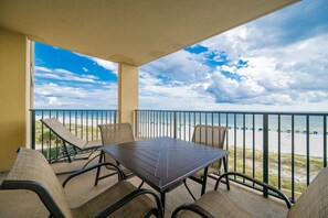 A balcony with a table and chairs, overlooking a beach with a view of the ocean and clouds. - Phoenix V 412 3 Bedroom Condo (Orange Beach)