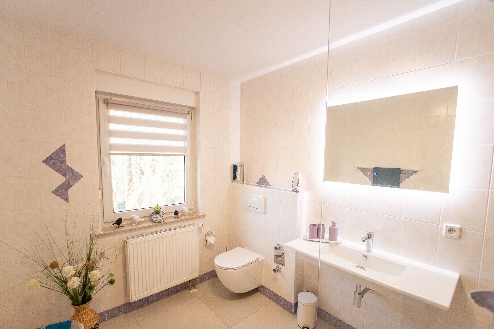 A bathroom with a toilet, sink, mirror, window, and radiator.