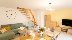 Ein modernes Wohnzimmer mit Essbereich, einer Treppe, einem Flachbildfernseher und einer Wanduhr.