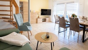 Ein modernes Wohnzimmer mit Sofa, Sesseln, Esstisch und Fernseher.