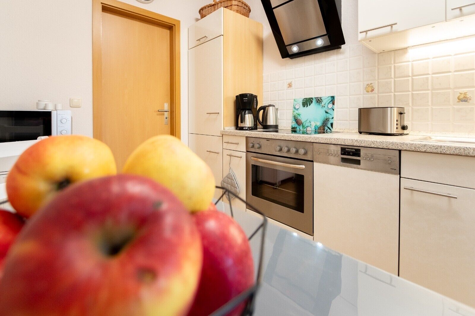 A kitchen with a microwave, stove, coffee maker, and a fruit bowl with apples.