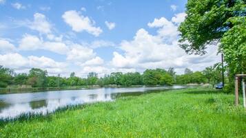 Ein ruhiger Fluss mit grünen Ufern und Bäumen, ein klarer Himmel und ein blaues Auto am Wasser geparkt.