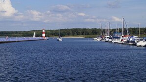 Ein Yachthafen mit vertäuten Booten, einem Leuchtturm und einem Sandstrand.