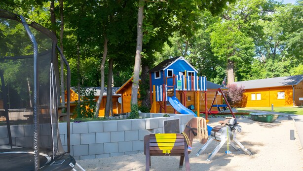 Ein Spielplatz mit Trampolin, Rutsche und Schaukel.