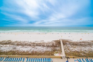 Een zandstrand met een steiger, strandparasols en ligbedden.