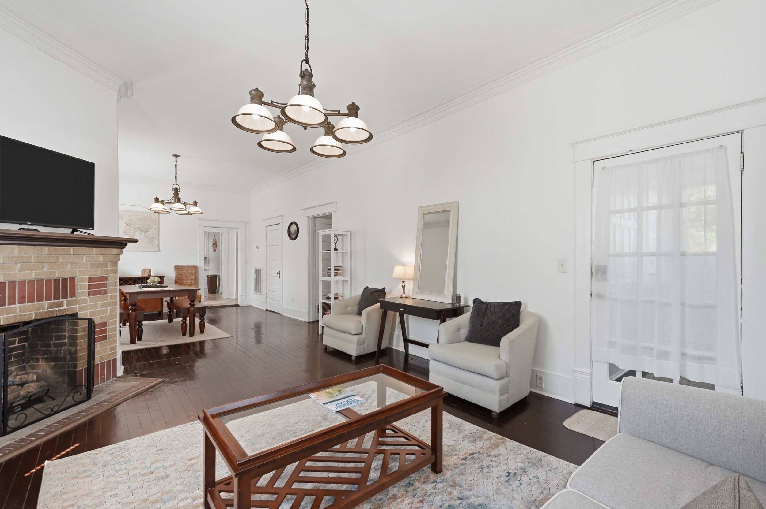 A living room with a fireplace, a television, a chandelier, and a dining area with a table and chairs.