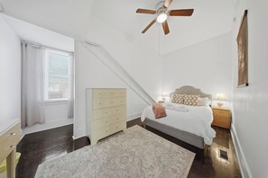 A bedroom with a bed, a dresser, a ceiling fan, a window with curtains, and a nightstand with a lamp. - Snipes-Taylor House: Historic Charm &Walk to DT! Huge porch and backyard! (Wilmington)