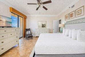 Une chambre d’hôtel avec un grand lit, un ventilateur de plafond, une commode, une chaise, une coiffeuse avec un miroir et des tableaux encadrés accrochés au mur.