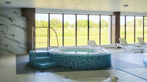 Una piscina amb un disseny mosaic, una terrassa solària amb gandules i grans finestres que ofereixen vistes a la vegetació.