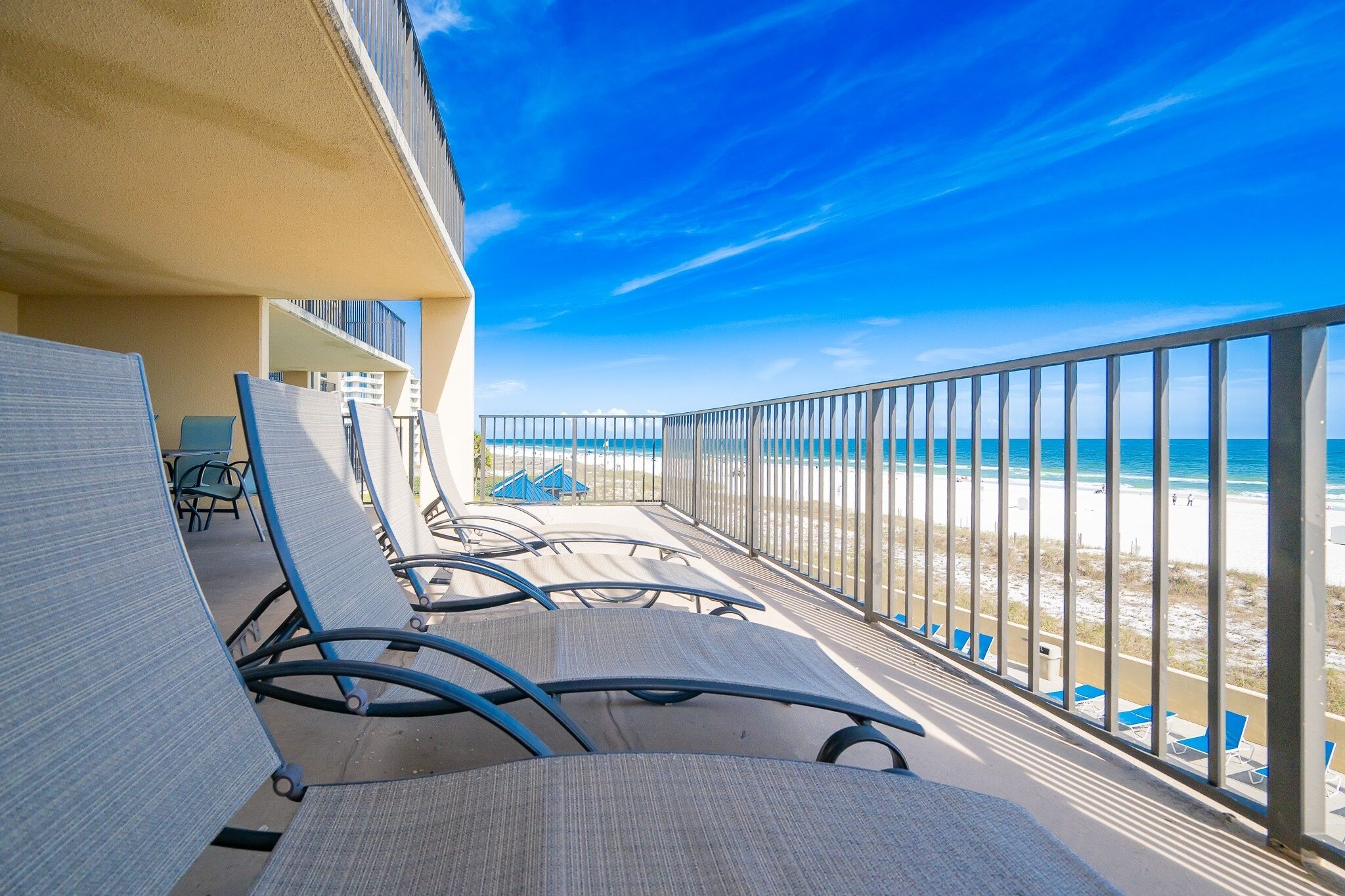 A balcony with chairs, a view of the beach, and a clear sky.