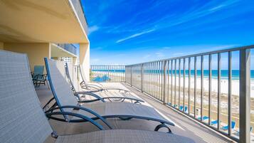 A balcony with chairs, a view of the beach, and a clear sky.