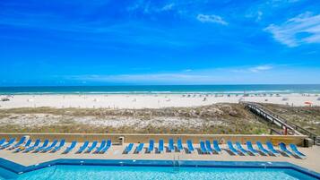 A pool with blue water, a beach with people, and a clear blue sky.