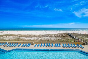 A pool with blue water, a beach with people, and a clear blue sky. - Phoenix V 209 2 Bedroom Condo (Orange Beach)