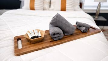A neatly made bed with a wooden tray holding toiletries and towels.