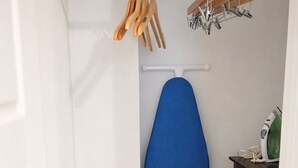 A small laundry room with a blue ironing board, a drying rack with wooden hangers, a storage bin, and a small cabinet with a green appliance. - Cozy Studio Downtown Detroit Steps from Wayne State University (Detroit)