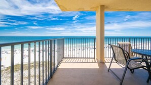 A balcony with a view of a beach, a table, and two chairs. - Phoenix V 817 3 Bedroom Condo (Orange Beach)