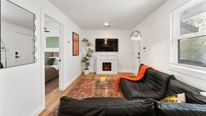 Un salon moderne avec une cheminée, un canapé en cuir noir, un téléviseur à écran plat et un grand miroir.