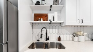 Une cuisine dotée d’un évier en acier inoxydable, de meubles blancs, d’une planche à découper en bois et d’un dosseret de carrelage blanc.