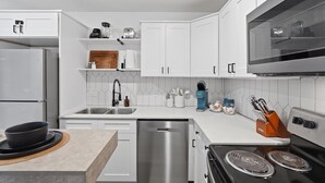 Une cuisine moderne avec des meubles blancs, des appareils en acier inoxydable, un lave-vaisselle et un four à micro-ondes.