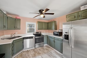 A kitchen with green cabinets, stainless steel appliances, a ceiling fan, and a window. - 5 Min to Notre Dame: Private Garage - Pet Friendly (South Bend)