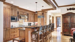 A spacious kitchen with wooden cabinets, a central island with bar stools, and a large wooden cabinet in the dining area. - 3BR Condo In Bachelor Gulch, Ski In/out (Avon)