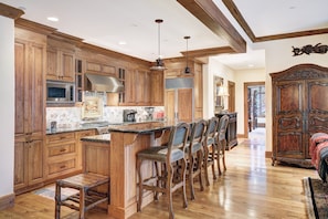 A spacious kitchen with wooden cabinets, a central island with bar stools, and a large wooden cabinet in the dining area. - 3BR Condo In Bachelor Gulch, Ski In/out (Avon)