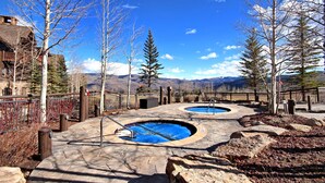 A pool area with two circular pools, surrounded by a stone deck and a wooden fence. - 3BR Condo In Bachelor Gulch, Ski In/out (Avon)