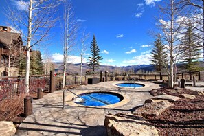 A pool area with two circular pools, surrounded by a stone deck and a wooden fence. - 3BR Condo In Bachelor Gulch, Ski In/out (Avon)