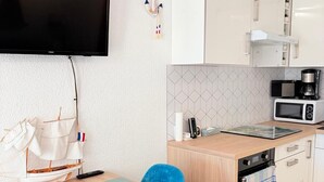 Una cocina compacta equipada con microondas, cafetera y horno pequeño. Hay una zona de comedor con mesa y sillas, y un televisor montado en la pared.