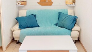Una sala de estar con un sofá blanco, dos cojines azules, una mesa de centro blanca, una decoración náutica de madera y un aire acondicionado instalado en la pared.
