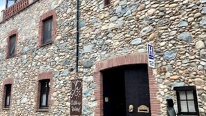 A stone building with a black entrance door, a signboard, and a metal sign indicating a restaurant. - Hotel Pasteral (La Cellera de Ter)