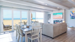 Un coin repas avec vue sur la plage, un salon doté d’une grande télévision et un mur en pierre.