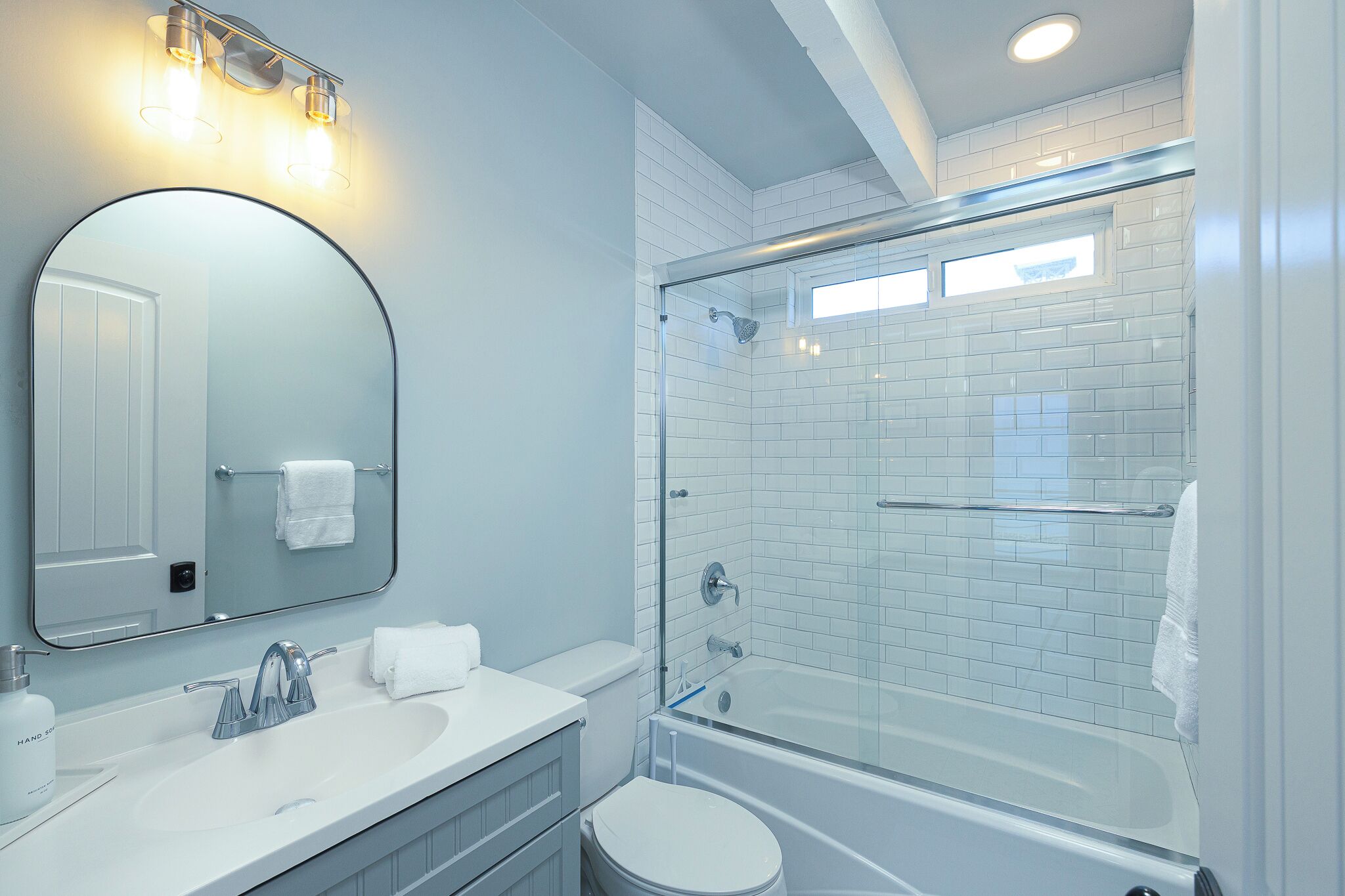 A modern bathroom with a glass-enclosed shower, a round mirror, and a white sink.