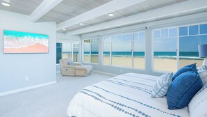 Une chambre avec une grande fenêtre, un lit, une chaise et un tableau.