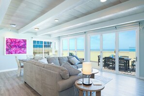A living room with a sofa, a table, and a lamp. There is a large window with a view of the beach.