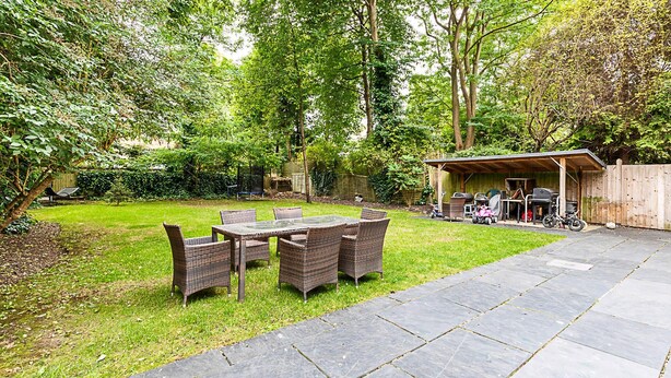 Eine Terrasse mit Tisch und Stühlen, umgeben von Rasen und Bäumen.