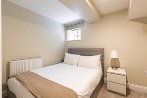 Ein Schlafzimmer mit Bett, Nachttisch, Lampe, Heizkörper und Fenster.