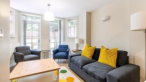 Ein Wohnzimmer mit einem grauen Sofa, zwei Sesseln, einem Holztisch und einer Lampe.