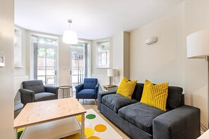 Ein Wohnzimmer mit einem grauen Sofa, zwei Sesseln, einem Holztisch und einer Lampe.
