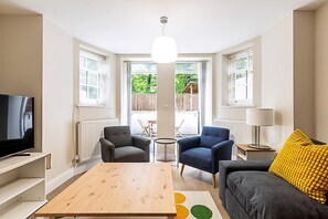 Ein modernes Wohnzimmer mit Fernseher, zwei Sesseln, einem Sofa, einem Holztisch und einer Lampe.