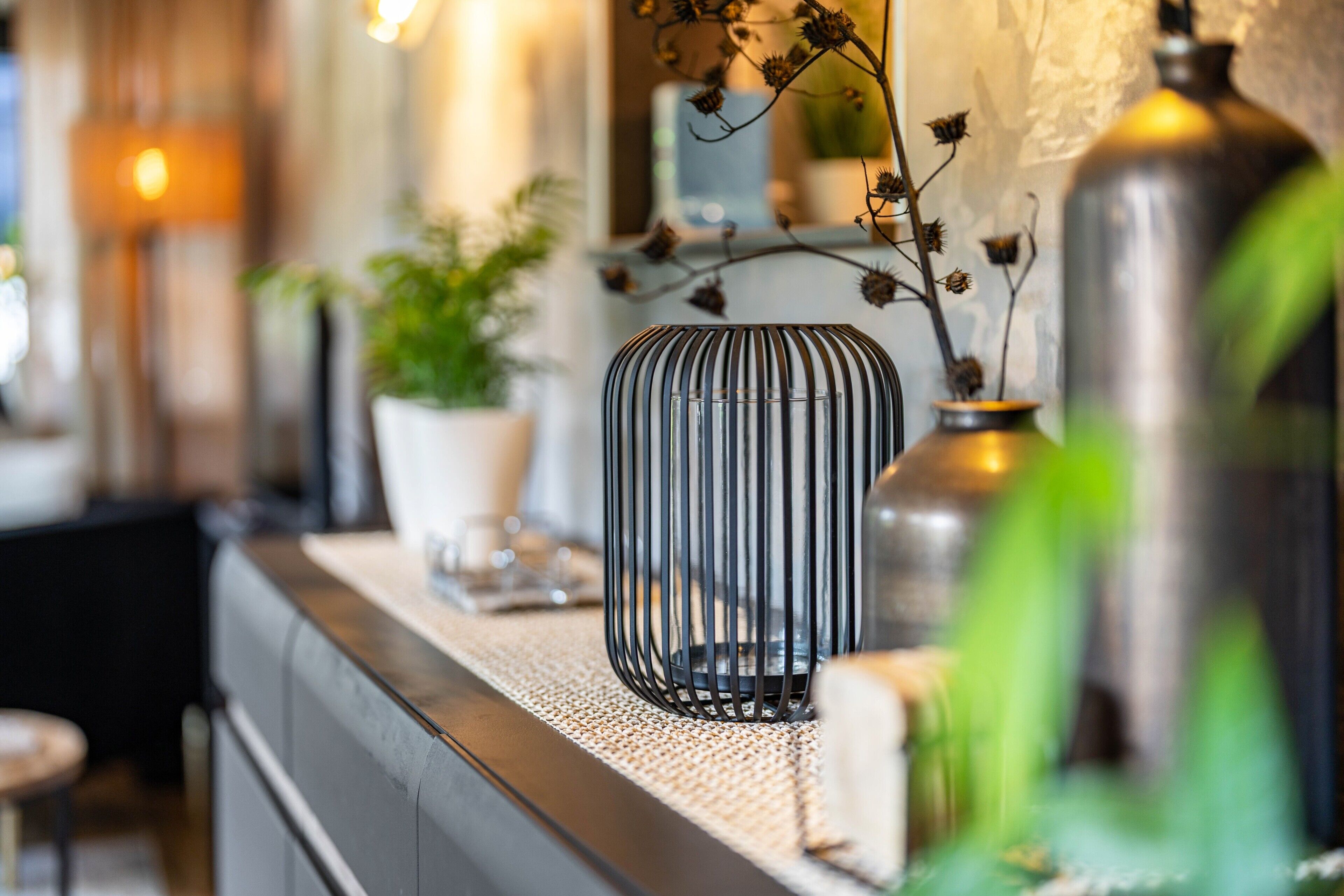 Un intérieur moderne avec un mur à texture, une plante en pot et un vase en métal posé sur une étagère.